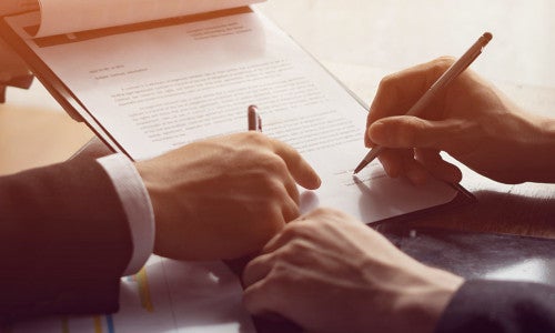 two people at desk, one signing contract