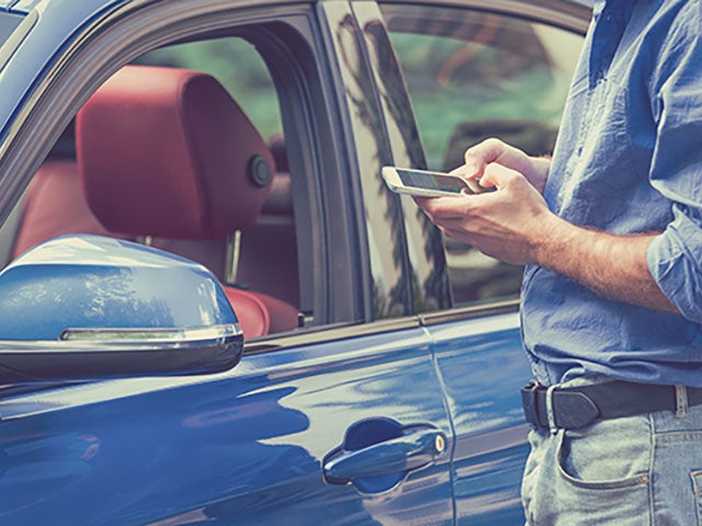 man standing outside of car dialing cell phone