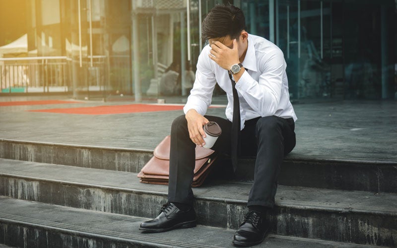 man in business suit sitting on steps holding head in hand