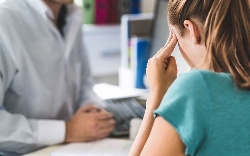 woman in doctors office putting hands on temples as if she has a headache