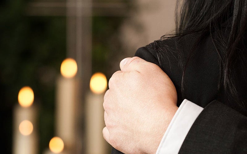 person's arm around another at a funeral