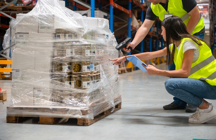 Warehouse workers investigating a damaged palette of canned olives.