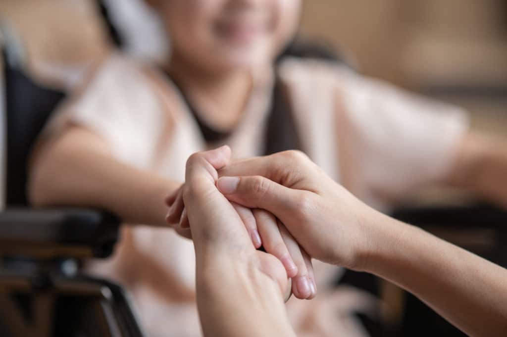 A woman holding the hand of her daughter in a wheelchair.