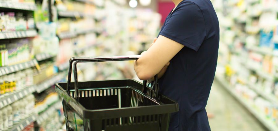 A close up of a woman with an empty shopping basket looking at the shelves of medication
