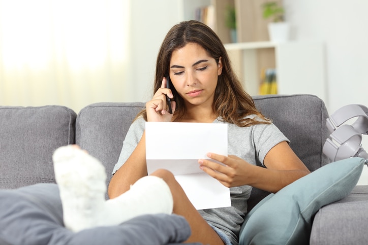 Woman with a broken leg calling on phone about a letter sitting on a couch in the living room at home