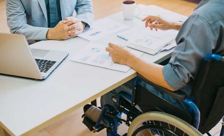 A close up of the hands on the desk of two men reviewing paperwork and one man is in a wheelchair