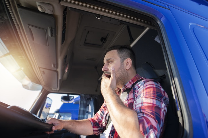 A truck driver yawning while driving.