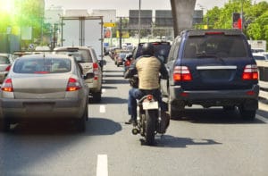 A motorcycle rider is viewed from behind as he sits waiting in a line of traffic