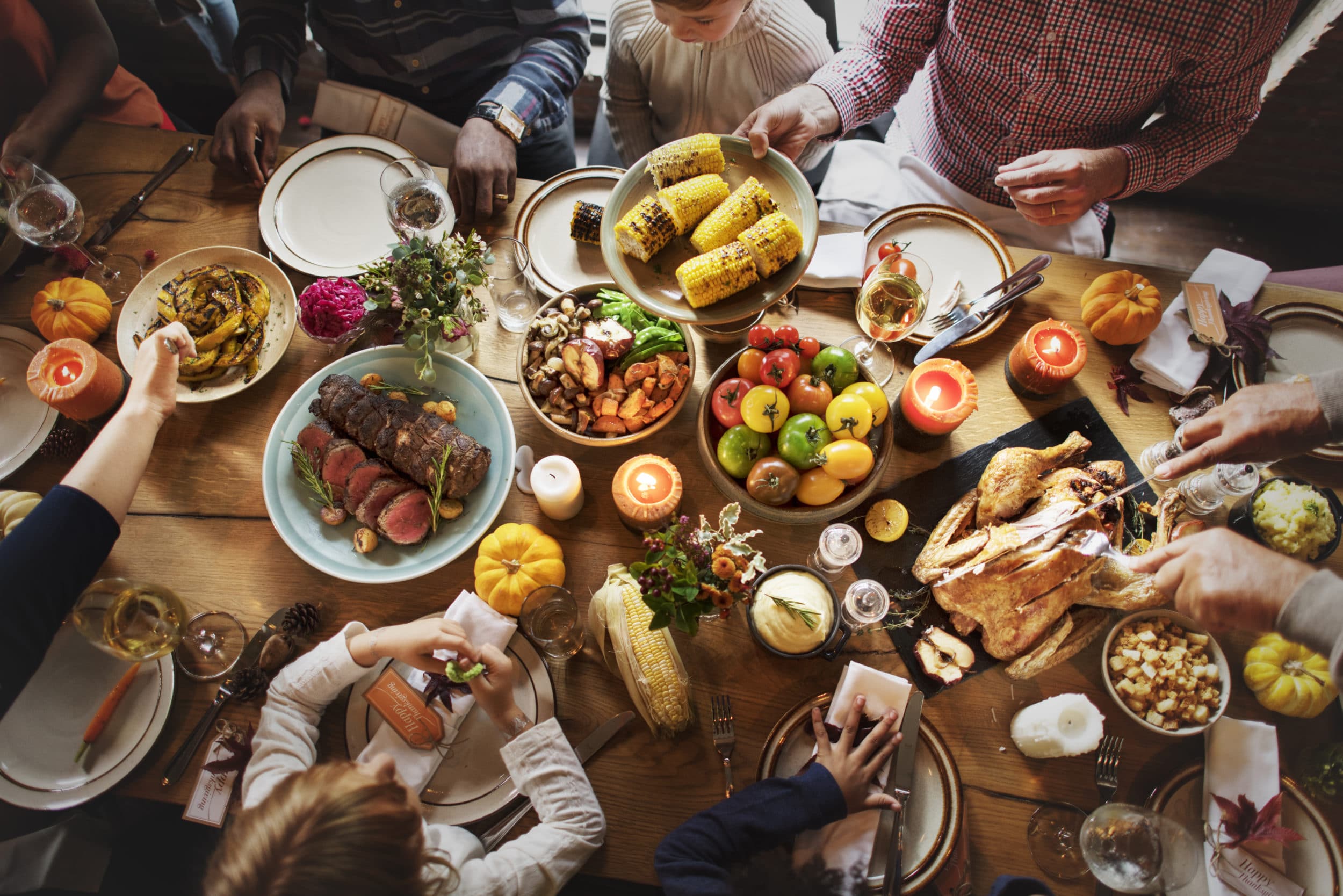 An aerial view of a family's full Thanksgiving table with people reaching in to serve themselves