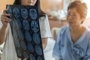 An older woman at a medical clinic sits on the treatment table and reviews a brain scan with a doctor