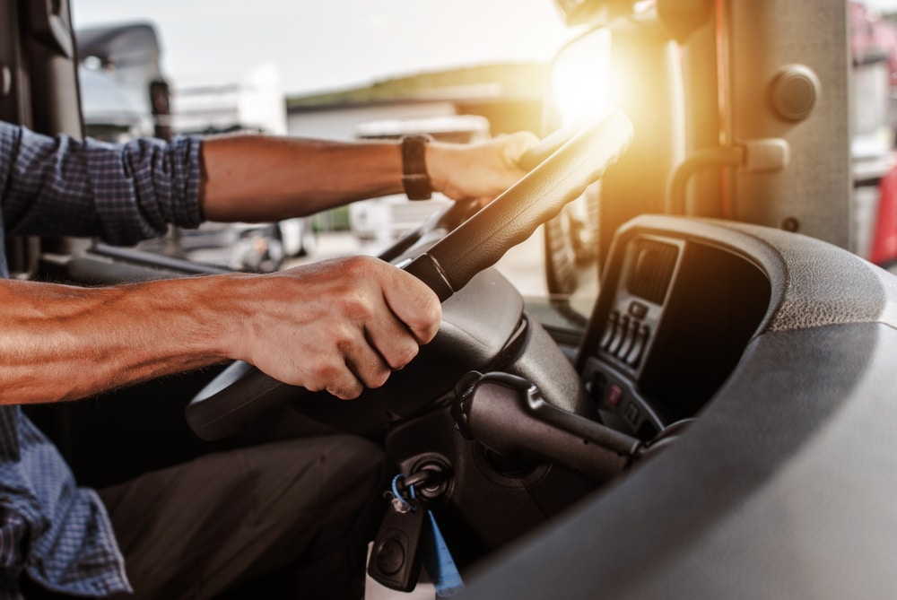 A close up of a man's hands on the steering wheel of a big rig