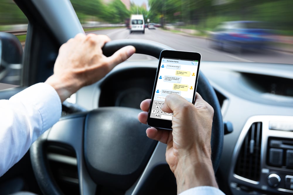 A close up of a man's hands using a cell phone to text while he is driving